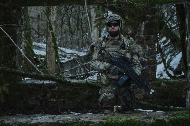 Portrait of airsoft player in professional equipment with machine gun in the forest. Soldier with weapons at war