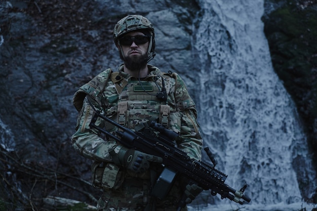 Portrait of airsoft player in professional equipment with machine gun in the forest. 