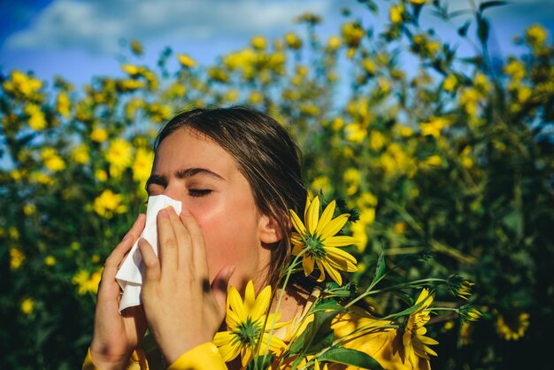 魅力的な明るい黄色のセーターを着て季節の花に囲まれたアレルギーの女性の肖像画