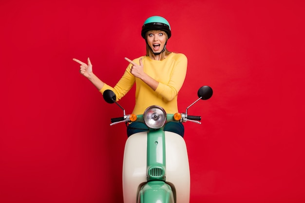 Portrait of amazed cheerful girl sitting on moped showing direct finger empty space