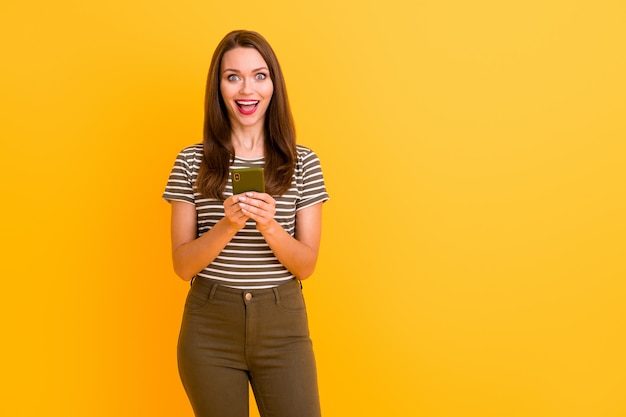 Portrait of amazed funky crazy girl use cell phone get social media notification about blog followers subscribers scream wow omg wear stylish clothes isolated over bright color wall