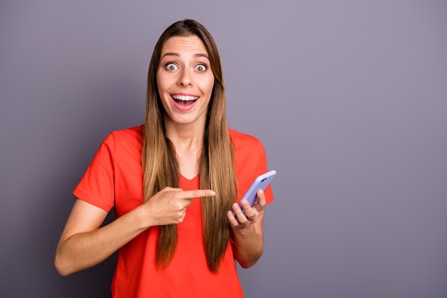 Portrait of amazed impressed brunette lady in red t-shirt posing against the purple wall