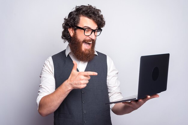 Portrait of amazed man wuith beard in suit pointing at his laptop.