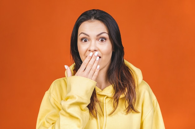 Portrait of amazed shocked young woman isolated over orange background.