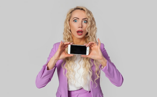 Портрет изумленной женщины, впечатление, показывающее экран смартфона, открытый рот