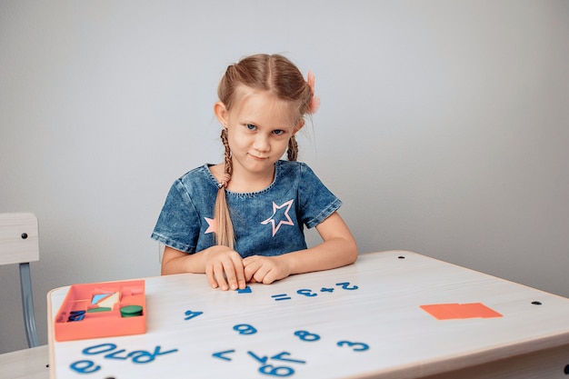 白いテーブルに座って数字を勉強している驚くべき美しい混乱した子供の肖像画。研究コンセプト。ノイズのある写真