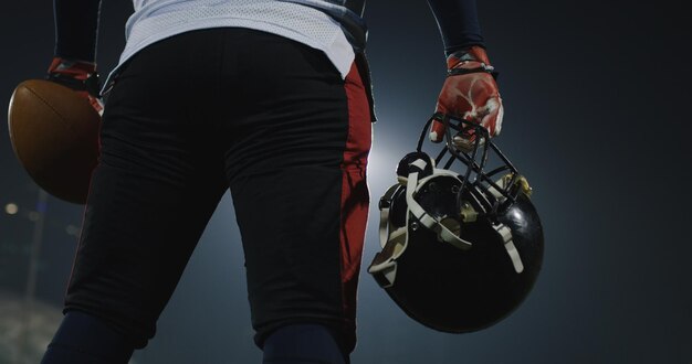 portrait of American Football player holding ball and helmet  rear view