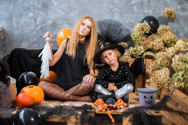 写真 肖像画、ハロウィーンの休日の装飾の中で、2歳の女の子が黒とオレンジの装飾の背景にカボチャを楽しんでいます