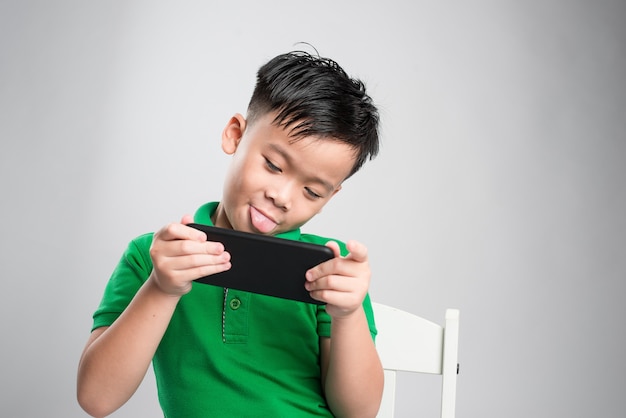 Portrait of an amused cute little kid playing games on smartphone isolated