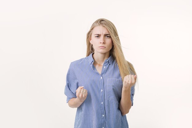 Portrait of angry blonde european girl dressed in blue striped shirt frowning face.