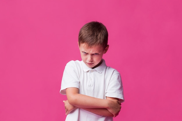 Photo portrait of angry boy standing over pink backdrop