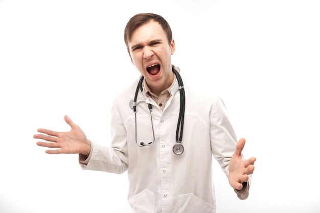 Portrait of angry doctor in white medical coat with stethoscope upset face screaming on white background with copy space