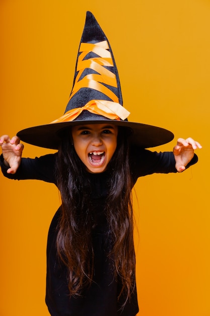 Portrait of an angry little girl in a witch costume, on a yellow background. halloween.