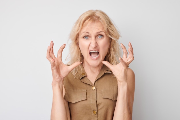 Portrait angry mature woman screaming and pretending to choke someone isolated on white studio background