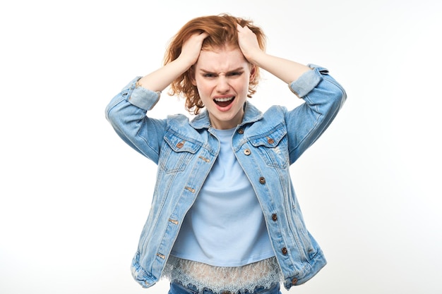 Портрет злой рыжеволосой молодой женщины, кричащей на белом студийном фоне, демонстрирующей негативные эмоцииxA