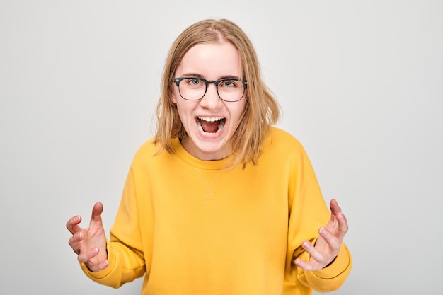 Portrait of angry schoolgirl yelling holding hands in furious gesture isolated on white studio background Devil face Human emotions facial expression concept