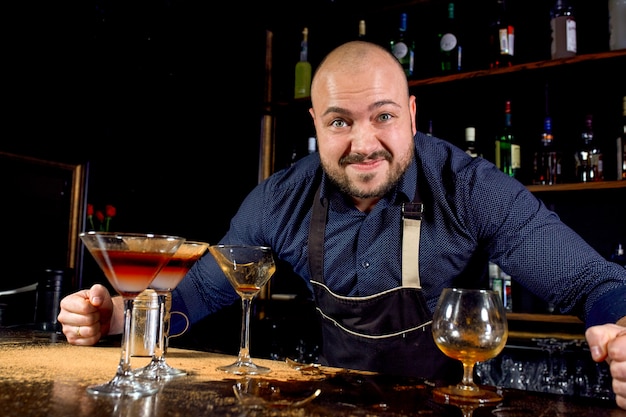 Portrait of angry and stressed barman with bowtie behind the bar with alcoholic drinks around. Stressful lifestyle of barista concept