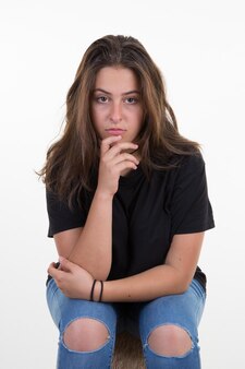 Ritratto di ragazza adolescente arrabbiata seduta con le braccia incrociate mano sul mento su sfondo bianco