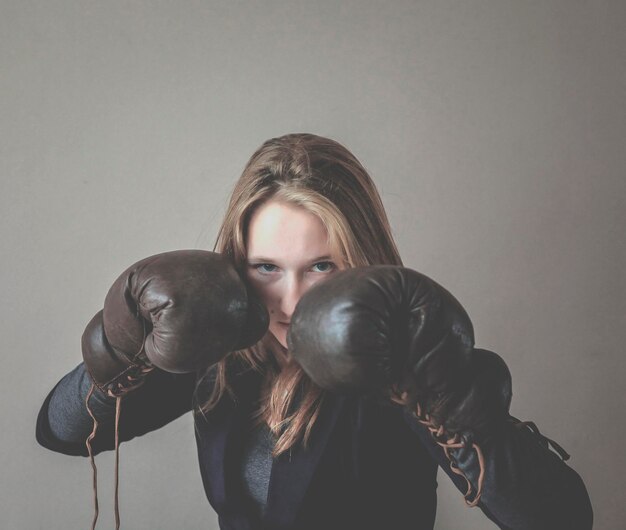 Photo portrait of angry woman wearing black boxing glove against gray background