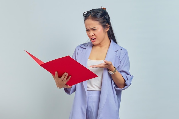 Photo portrait of angry young asian business woman in suit standing pointing at document folder with palms isolated on purple background