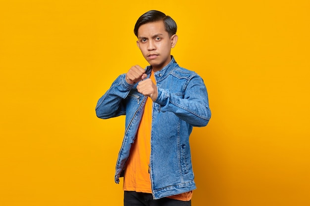 Portrait of angry young asian man showing boxer gesture on yellow background