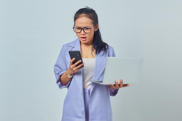 Portrait of angry young Asian woman looking at message on smartphone and holding laptop, knowing canceled job isolated on white background