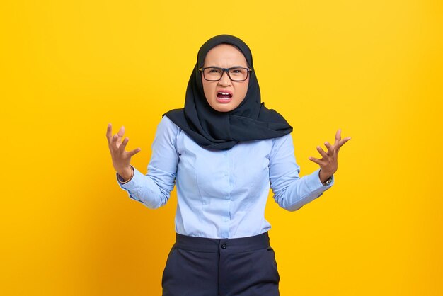 Portrait of angry young asian woman shouting and gesturing with hands isolated on yellow background