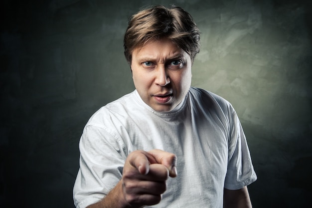 Photo portrait of angry young man pointing at you over gray background