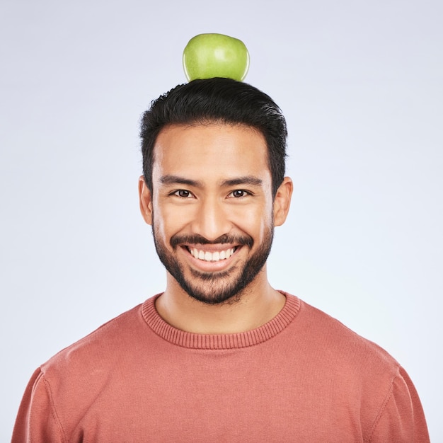 写真 肖像画のリンゴの頭のバランスと減量ダイエットのための男性の笑顔健康的なスナックや体の栄養ビタミン白い背景に食べ物栄養士の果物と空腹のアジア人のスタジオの顔を食べる