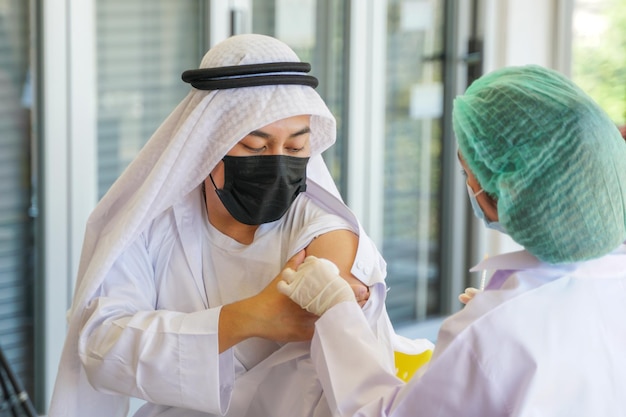 Portrait of Arab Muslim man looking at while getting covid vaccine in clinic or hospital, with hand nurse injecting vaccine to get immunity for protect virus. people wearing protective mask.