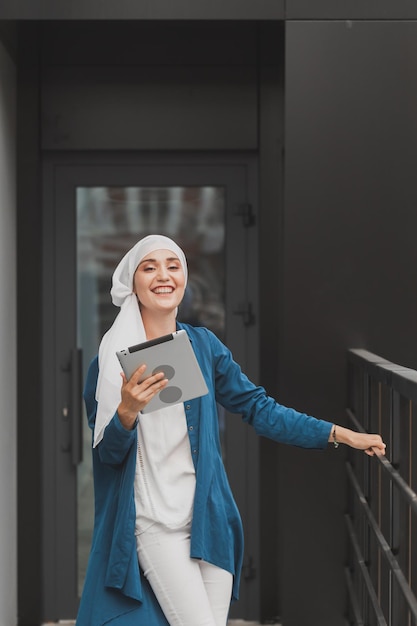 태블릿을 들고 있는 아랍 학생 소녀의 초상화. 거리에서 태블릿을 들고 히잡을 쓴 아랍 비즈니스 여성. 여자는 히잡을 입고 있다.