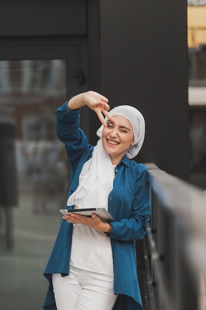 Portrait of an Arab student girl holding a tablet. Arab business woman in hijab holding a tablet in the street. Woman is dressed in hijab