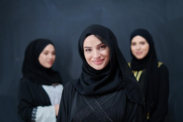 Portrait of Arab women wearing traditional clothes or abaya. Young muslim girls posing in front of black chalkboard representing islamic arabic fashion and ramadan kareem concept