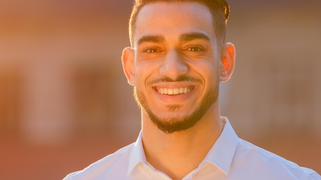 Portrait arabic hispanic man businessman ethnic bearded guy\
wears formal shirt stands posing outdoors in street in sun sunset\
looking at camera smiling toothy dental waving head yes nods\
positively