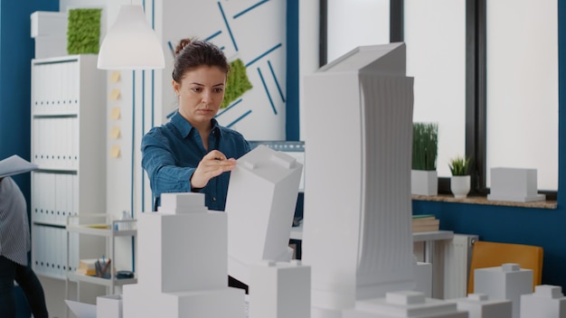 Portrait of architect looking at building model and maquette to\
plan urban project in office. woman engineer working on\
construction design and layout to create real estate property.