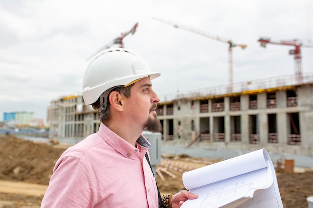 Foto ritratto di architetto al lavoro con casco in un cantiere edile, legge il piano.