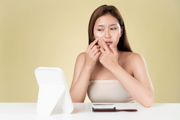 Portrait of ardent asian woman looking at mirror worry about pimple