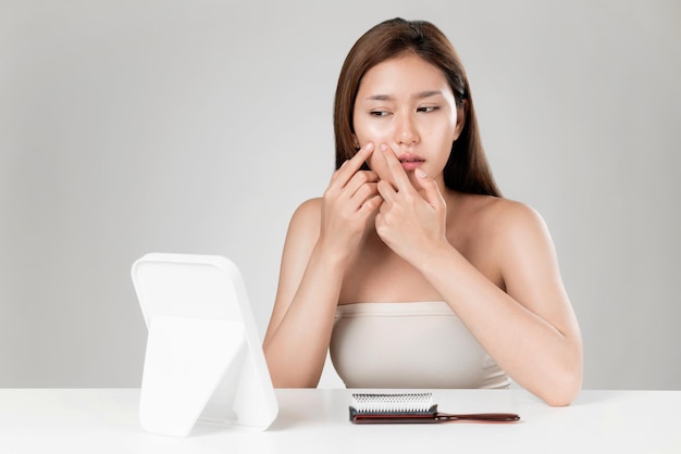 Portrait of ardent asian woman looking at mirror worry about pimple