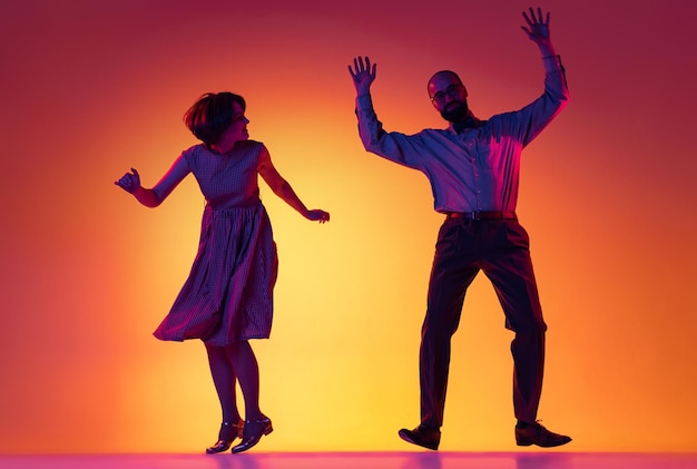 Photo portrait of artistic couple dancing retro style dance isolated over gradient orange yellow background in neon light