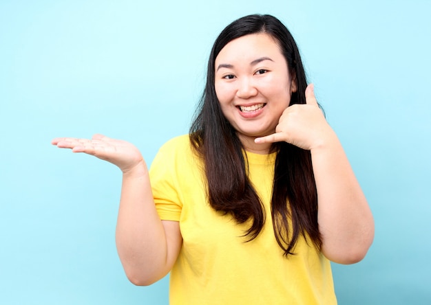 Portrait Asia woman is pretending to answer the phone to invite, isolated on blue background in studio.