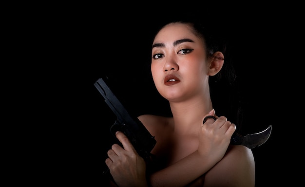 黒い背景に銃とカランビットナイフを持っている肖像画アジアの女性片手ヨン