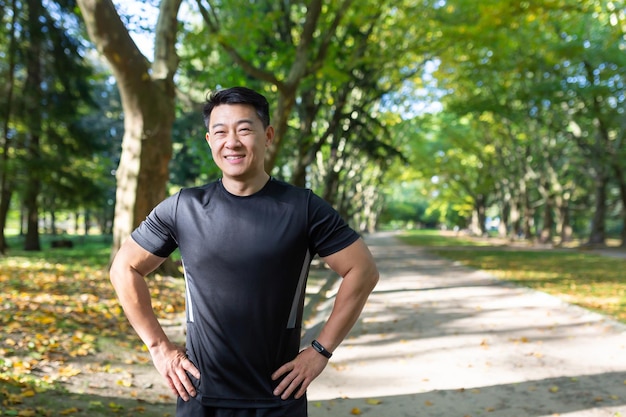 Portrait of asian athlete in autumn park on sunny day man in sportswear smiling and looking at