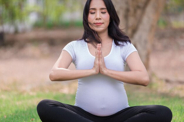 公園でアジアの美しい妊婦の肖像タイの人々幸せな女性のコンセプト彼女は芝生でヨガをします