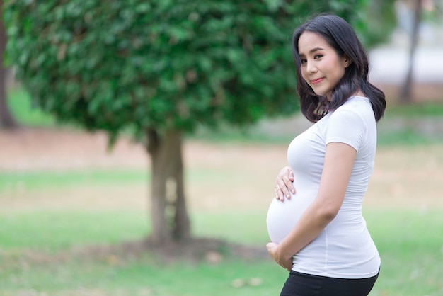 Portrait of asian Beautiful pregnant woman at the parkThailand peopleHappy woman conceptHer use hand touch her bellyMother day concept