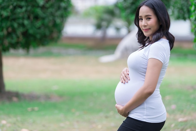 Portrait of asian Beautiful pregnant woman at the parkThailand peopleHappy woman conceptHer use hand touch her bellyMother day concept