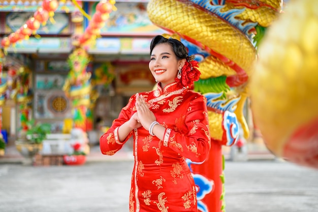 中国の旧正月の神社で笑顔とおめでとうのジェスチャーでポーズをとってチャイナドレスを着ている肖像画アジアの美しい女性