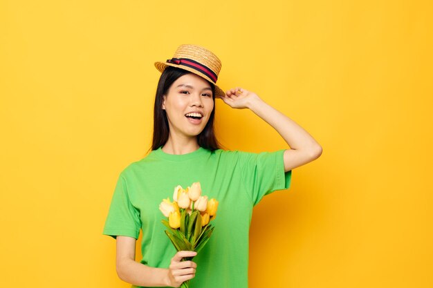 Portrait Asian beautiful young woman posing with a bouquet of flowers in a hat yellow background unaltered