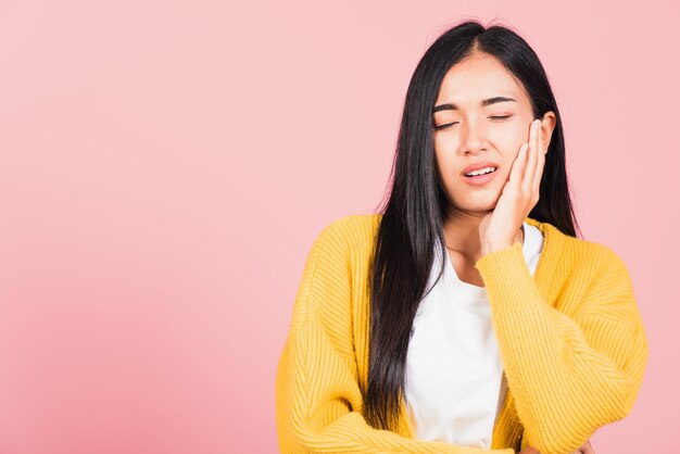 Portrait of Asian beautiful young woman suffering from toothache, female terrible strong teeth pain problem pressing hand to chin, studio shot isolated on pink background, Dental health care concept