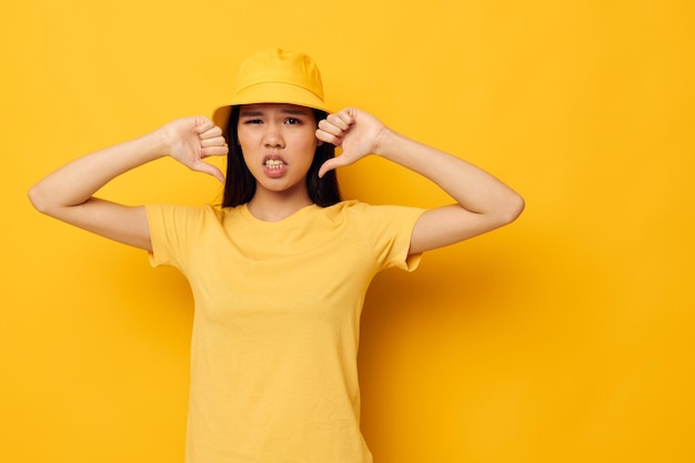 Portrait Asian beautiful young woman in a yellow tshirt and hat posing emotions yellow background unaltered