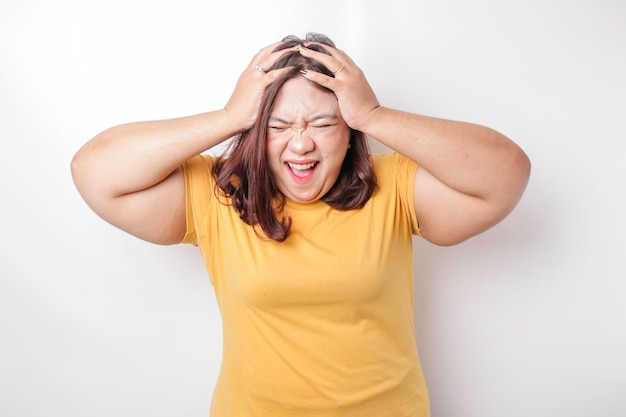 A portrait of an Asian big sized woman wearing a yellow tshirt isolated by white background looks depressed